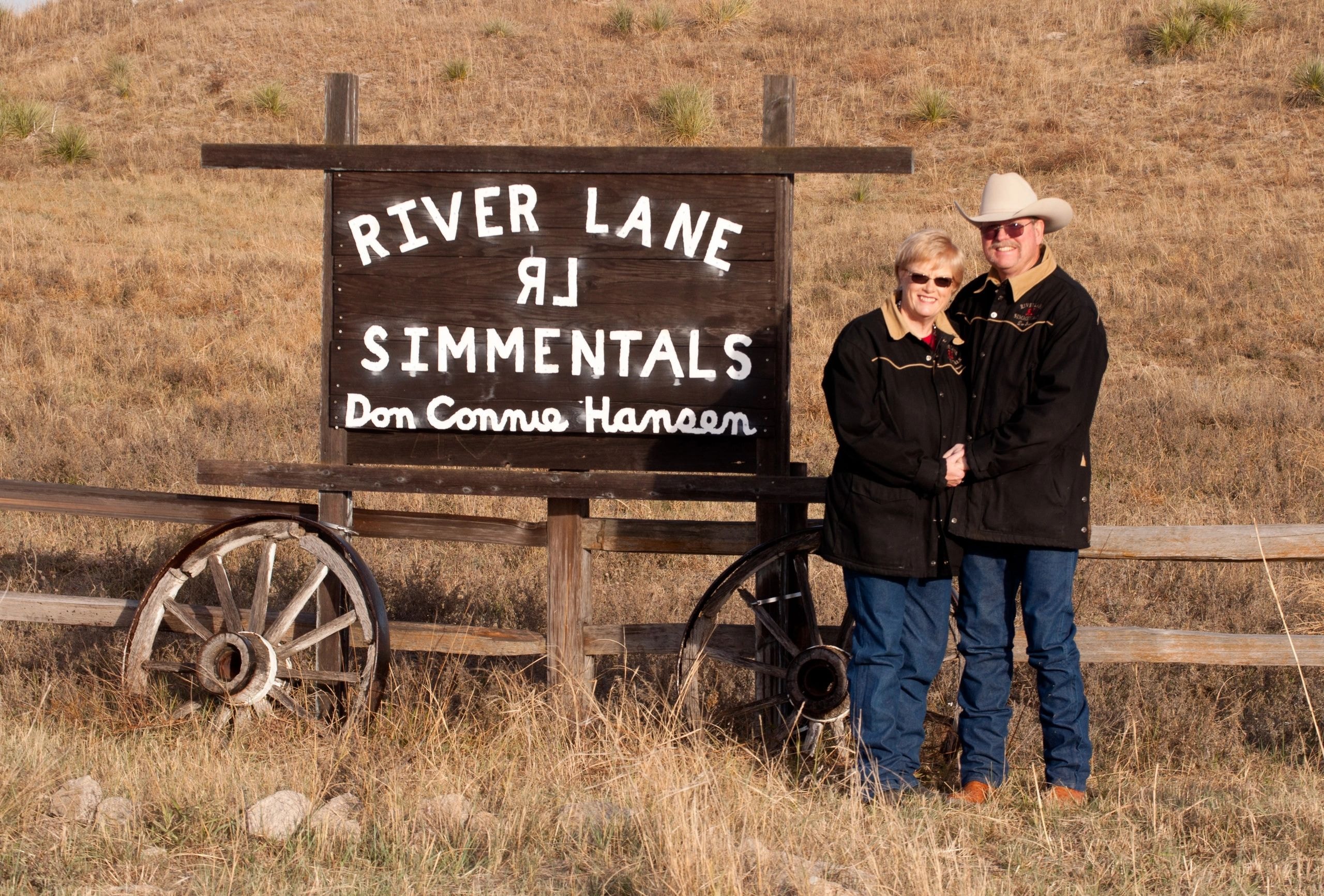 Don and Connie Hansen standing beside the River Lane Simmentals ranch sign
